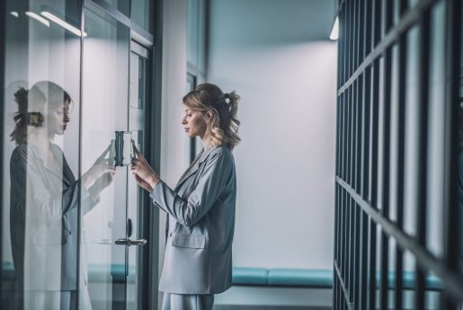 Reading code. Young confident business woman holding smartphone to combination lock on office door in building
